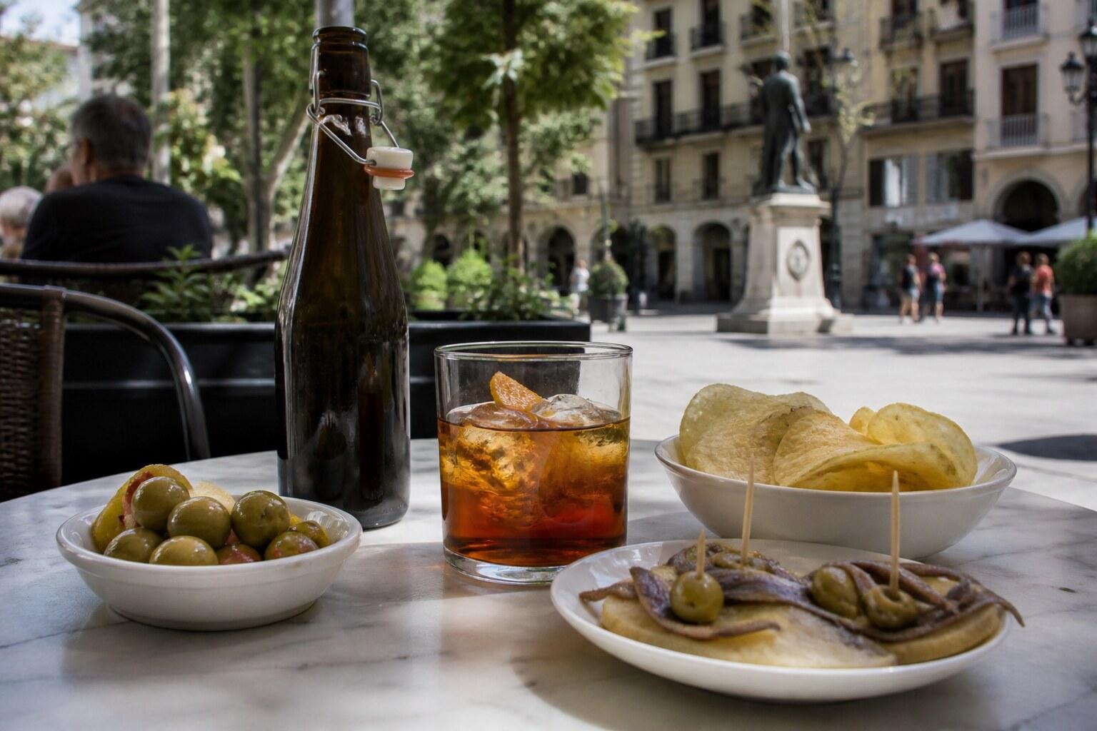 Glass of amber vermouth with olives, potato chips, and anchovy bites on a café table