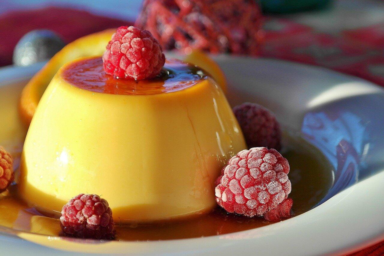Golden egg flan turned onto a plate with caramel sauce and raspberries